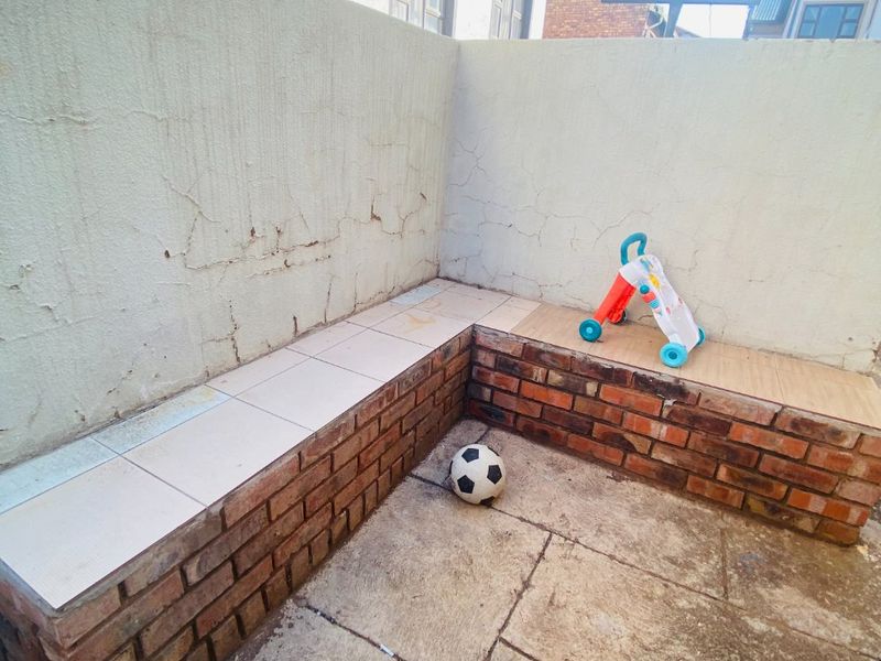 Outdoor patio area featuring a brick built-in bench with tiled seating, requiring some maintenance to the wall plaster and paving.