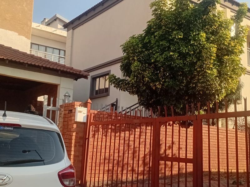 Front view of a double-storey residential property featuring a brick boundary wall, metal security gate, and a tiled roof structure.