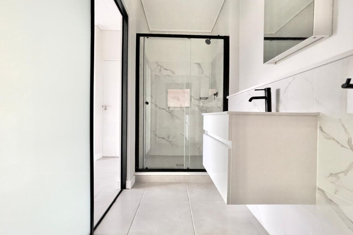 Modern bathroom featuring a floating vanity, black fixtures, and a glass-enclosed shower with marble-look wall tiling.