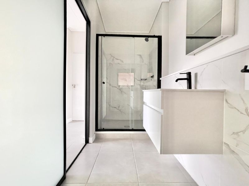 Modern bathroom featuring a floating vanity, black fixtures, and a glass-enclosed shower with marble-look wall tiling.