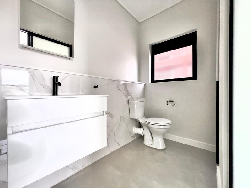 Modern bathroom featuring a sleek wall-mounted vanity, marble-look tiled splashback, black fixtures, and a clean, minimalist aesthetic.