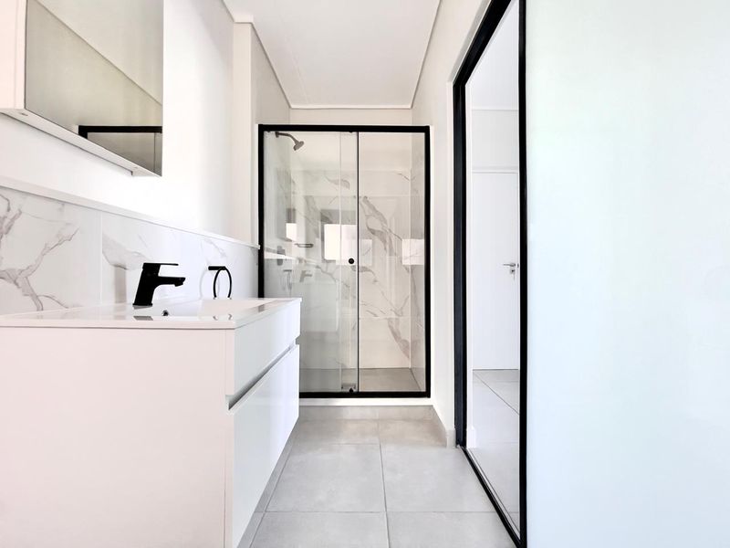 Modern bathroom featuring a sleek white vanity, black fixtures, and a glass-enclosed shower with marble-look wall tiling.