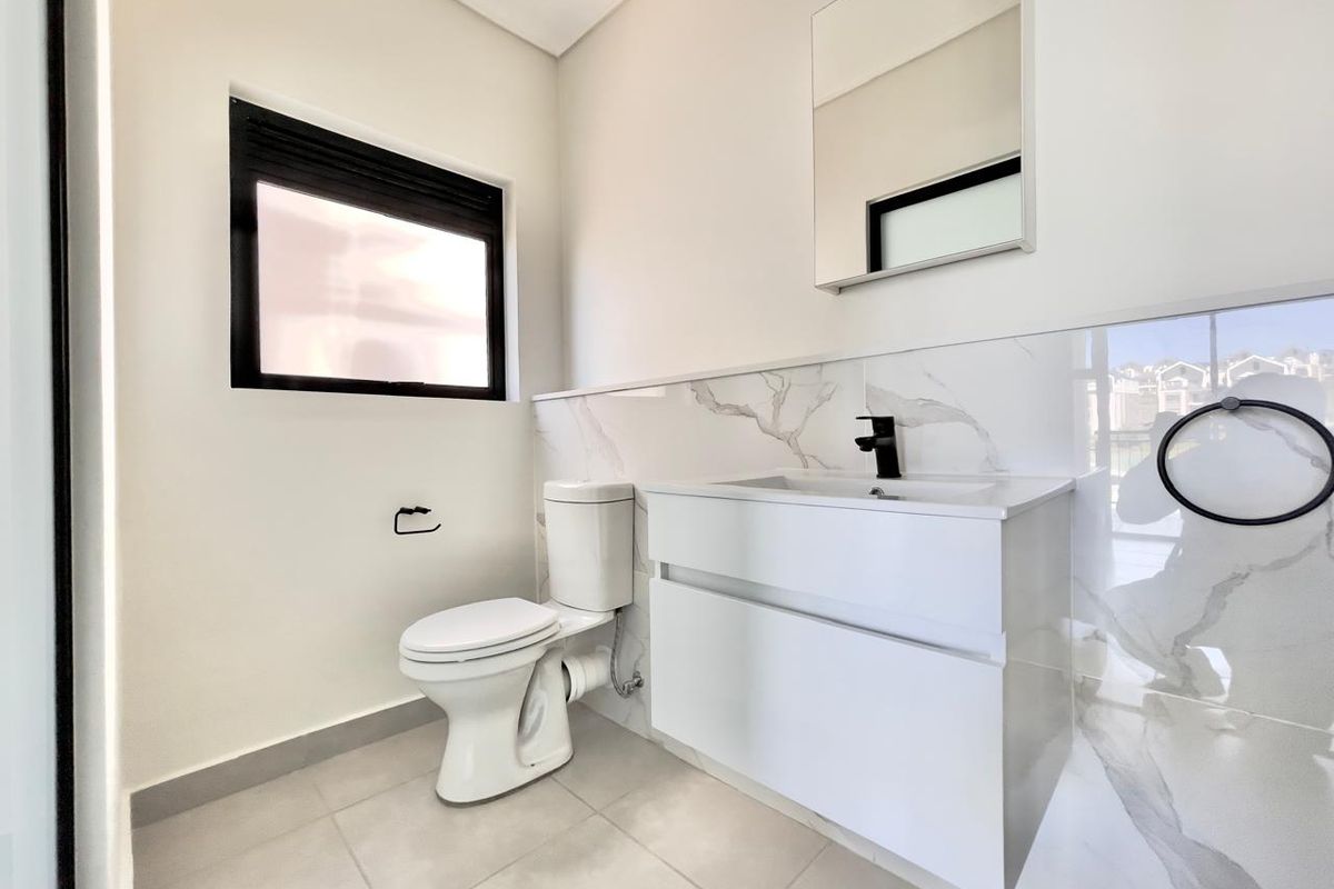 A modern, clean bathroom featuring a sleek vanity with a black faucet, marble-look wall tiling, and a wall-mounted mirror.