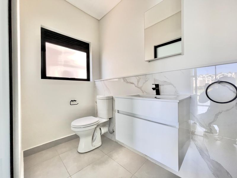 A modern, clean bathroom featuring a sleek vanity with a black faucet, marble-look wall tiling, and a wall-mounted mirror.