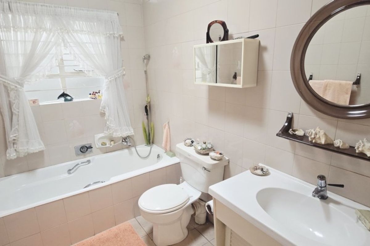 A functional bathroom featuring a built-in bathtub, wall-mounted vanity basin, toilet, and tiled finishes throughout.