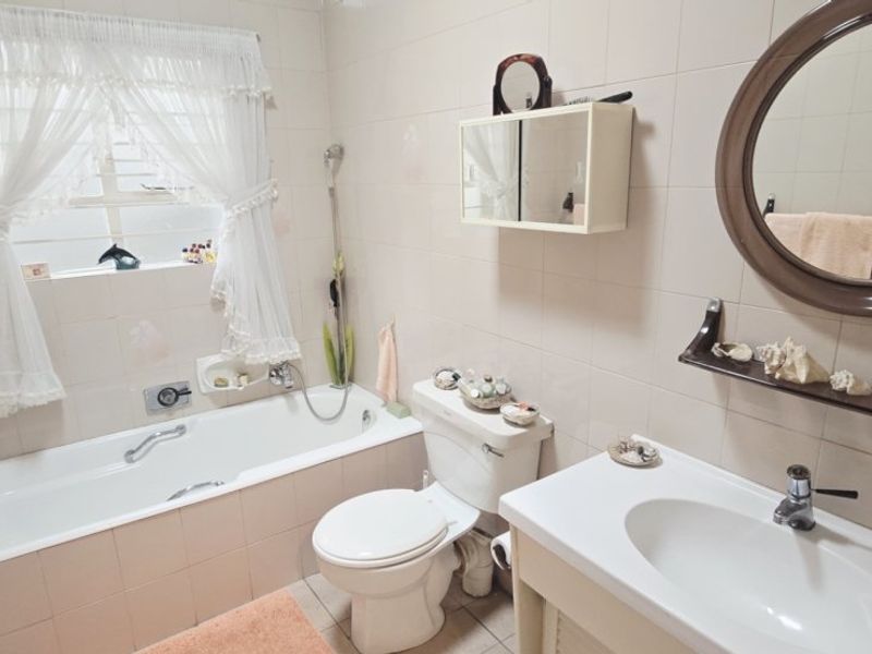 A functional bathroom featuring a built-in bathtub, wall-mounted vanity basin, toilet, and tiled finishes throughout.