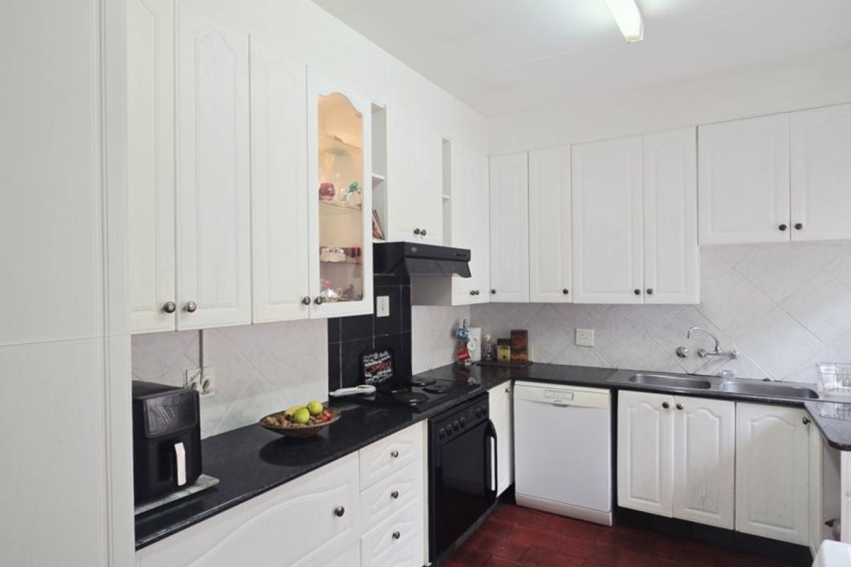 A functional kitchen featuring white cabinetry, dark granite countertops, a tiled backsplash, and integrated appliances including an oven and extractor fan.