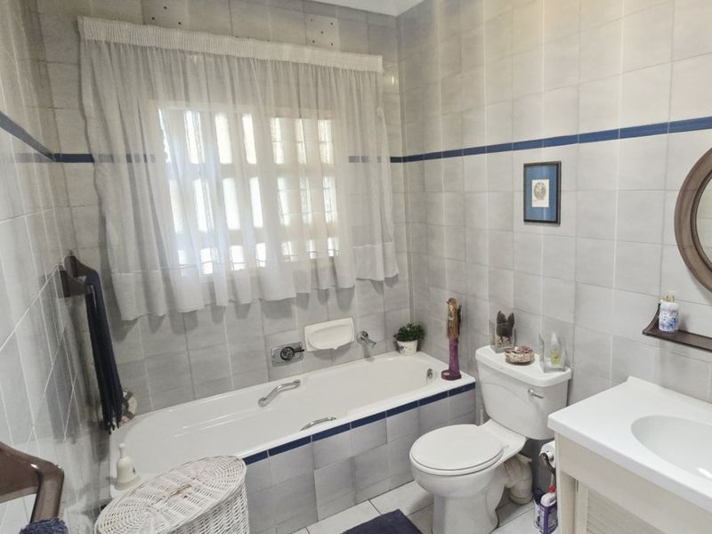 A functional bathroom featuring a bathtub, toilet, and vanity basin with neutral wall and floor tiling throughout.