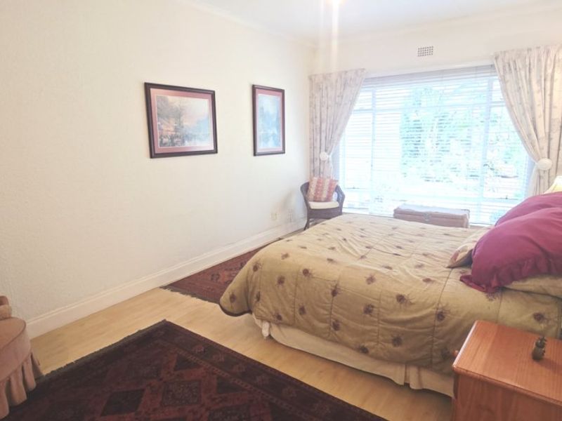 A well-lit bedroom featuring laminate flooring and a large window, providing a comfortable and functional living space.