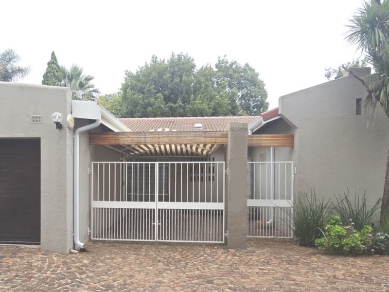 Front elevation of the apartment featuring a single garage, paved driveway, and a secure gated entrance with a timber pergola.