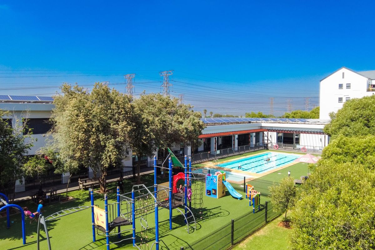 Aerial view of a communal apartment complex featuring a swimming pool, playground area, and landscaped grounds with solar panels installed on the roof.