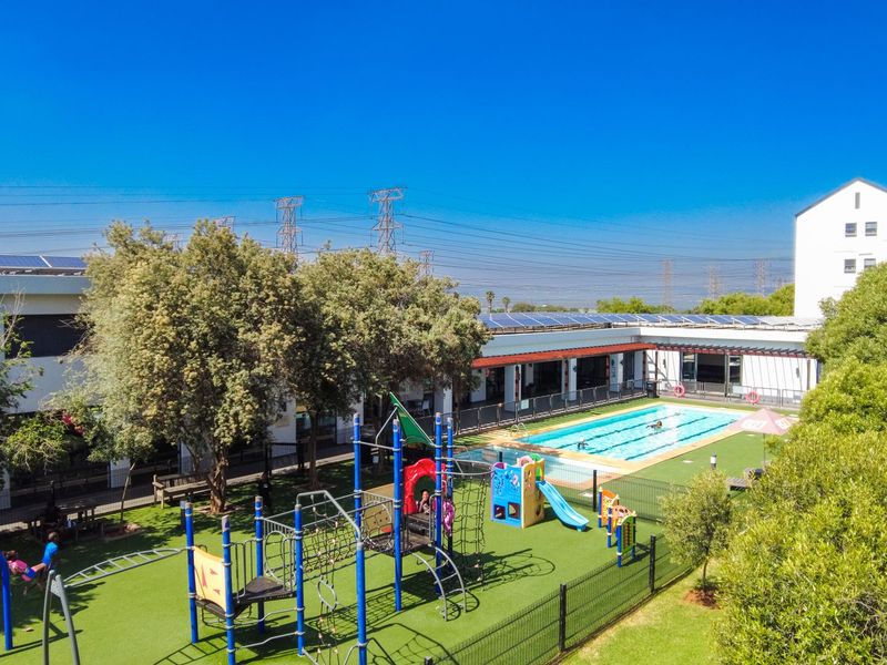 Aerial view of a communal apartment complex featuring a swimming pool, playground area, and landscaped grounds with solar panels installed on the roof.
