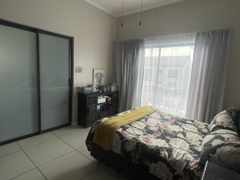 A well-lit bedroom featuring tiled flooring, a modern sliding door wardrobe, and direct access to a balcony through large sliding glass doors.