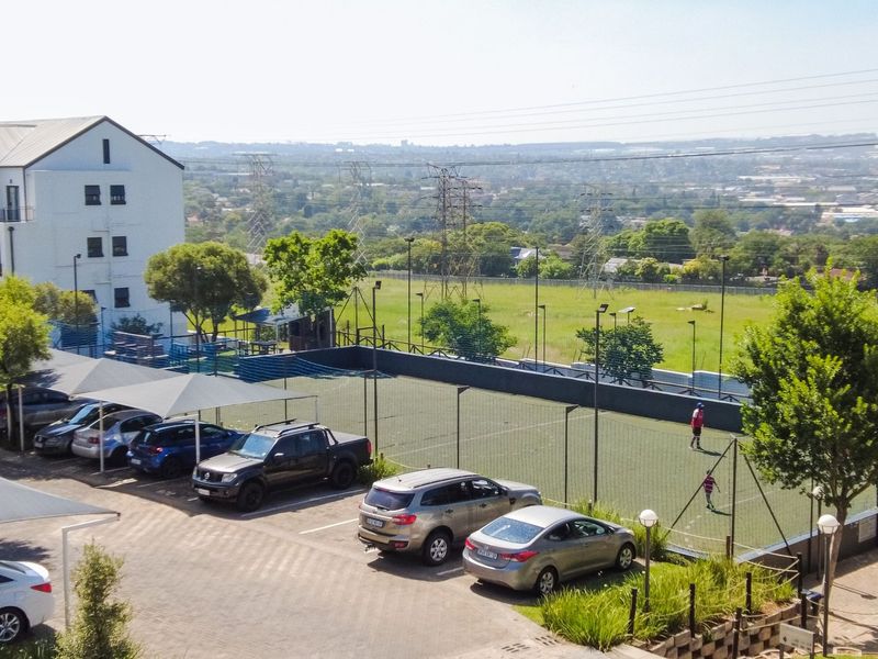 Aerial view of the apartment complex featuring a fenced sports court and covered parking bays with shade cloth structures.