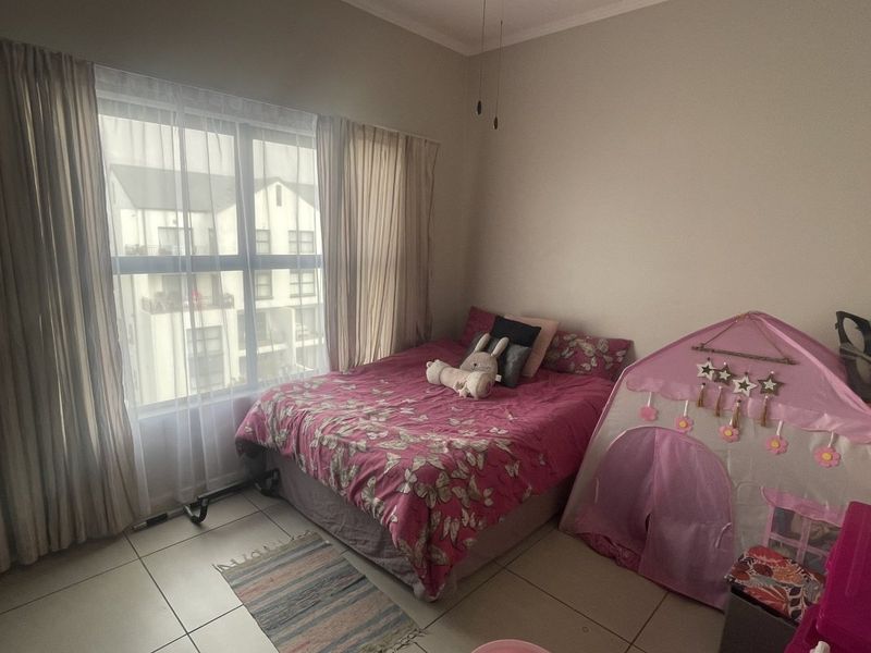 A bedroom featuring tiled flooring and a large window providing natural light, suitable for a child's room or guest bedroom.