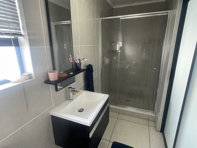A modern bathroom featuring a vanity basin, a glass-enclosed shower, and neutral wall and floor tiling.
