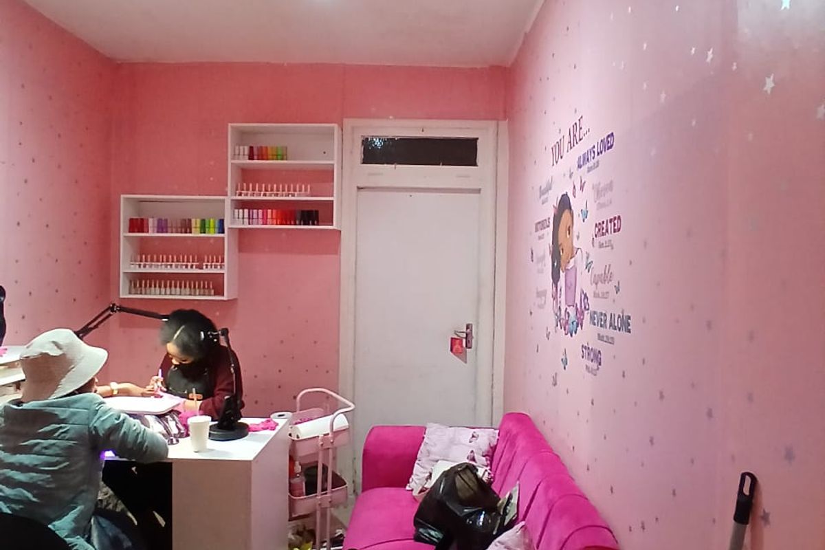 A small commercial office space currently utilized as a nail salon, featuring built-in wall shelving and track lighting.