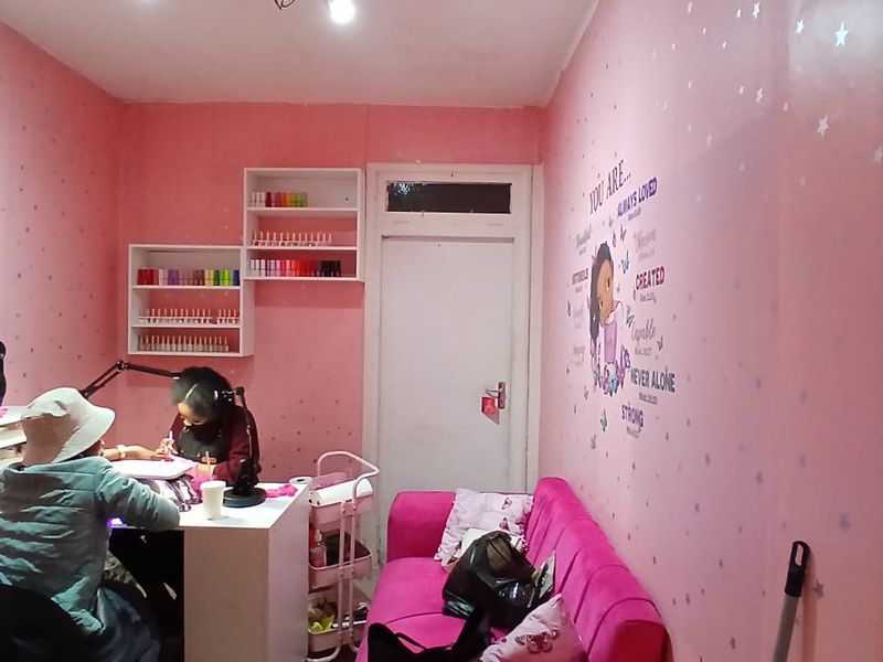 A small commercial office space currently utilized as a nail salon, featuring built-in wall shelving and track lighting.