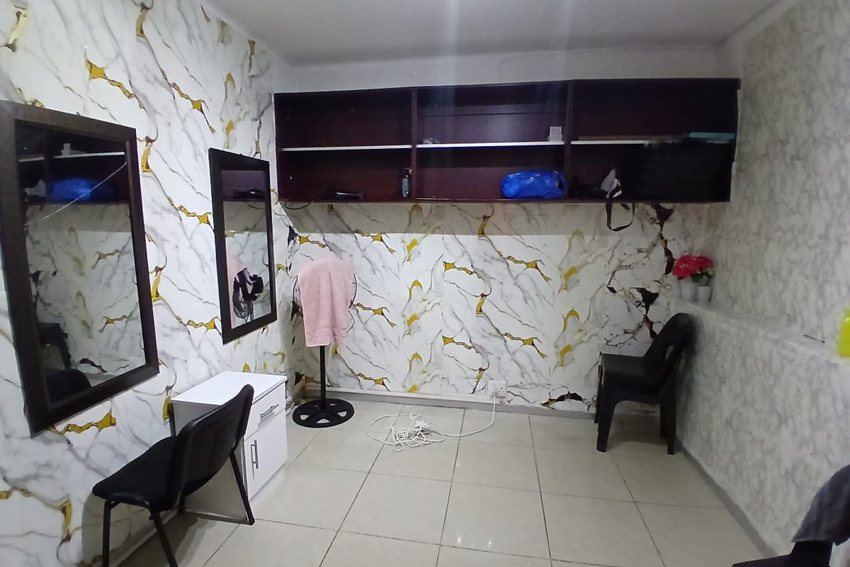 A small commercial office space featuring tiled flooring, built-in overhead shelving, and wall-mounted mirrors, currently showing signs of wear on the wall finishes.