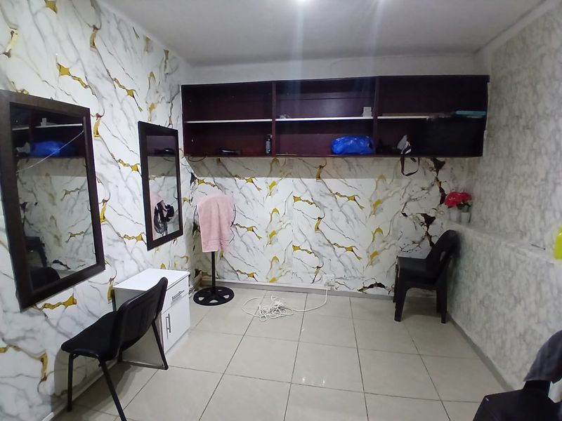 A small commercial office space featuring tiled flooring, built-in overhead shelving, and wall-mounted mirrors, currently showing signs of wear on the wall finishes.