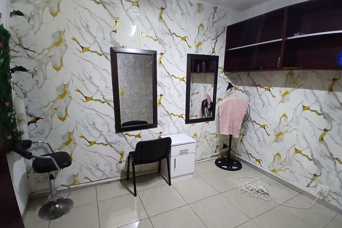 A utility or salon-style workspace featuring tiled floors, wall-mounted mirrors, and built-in overhead shelving with decorative marble-effect wall paneling.