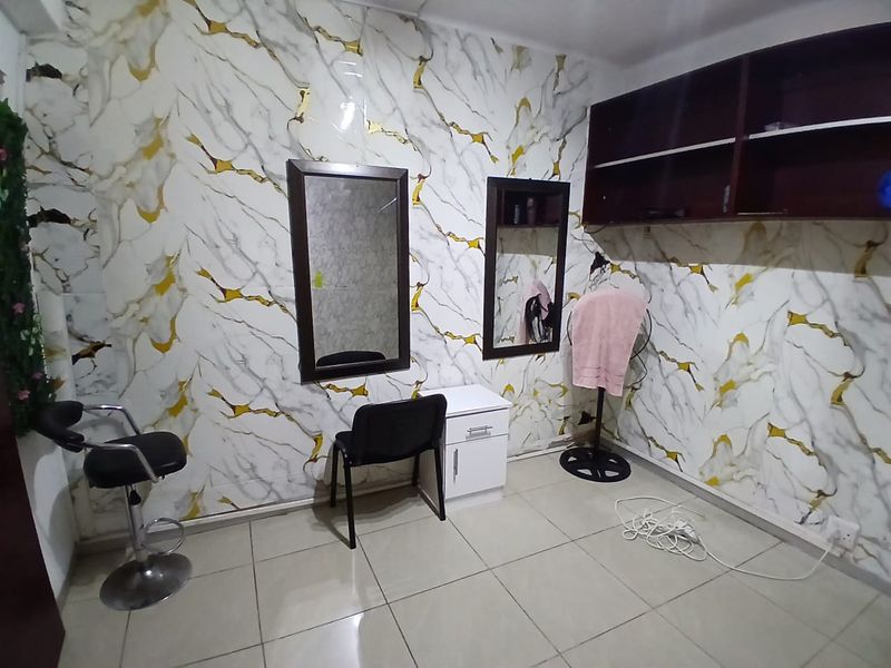 A utility or salon-style workspace featuring tiled floors, wall-mounted mirrors, and built-in overhead shelving with decorative marble-effect wall paneling.
