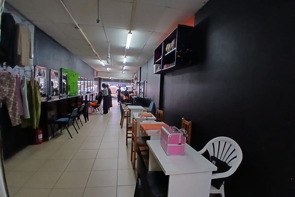 Open-plan commercial space featuring tiled flooring, fluorescent lighting, and wall-mounted shelving, suitable for a salon or retail environment.