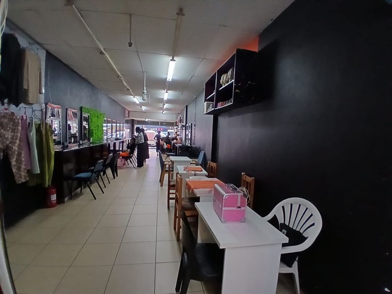 Open-plan commercial space featuring tiled flooring, fluorescent lighting, and wall-mounted shelving, suitable for a salon or retail environment.
