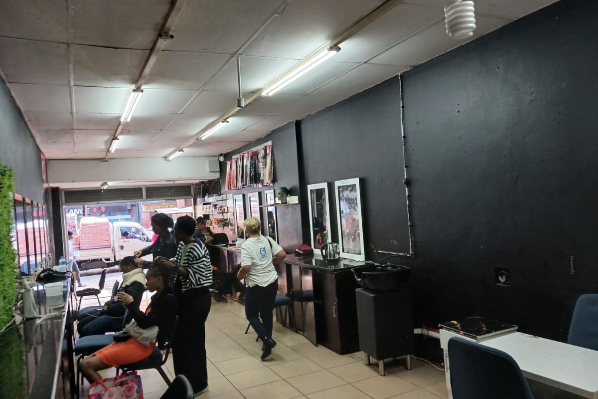 Commercial salon space featuring tiled flooring, drop ceiling, built-in vanity mirrors, and a plumbed wash basin, suitable for beauty or retail operations.