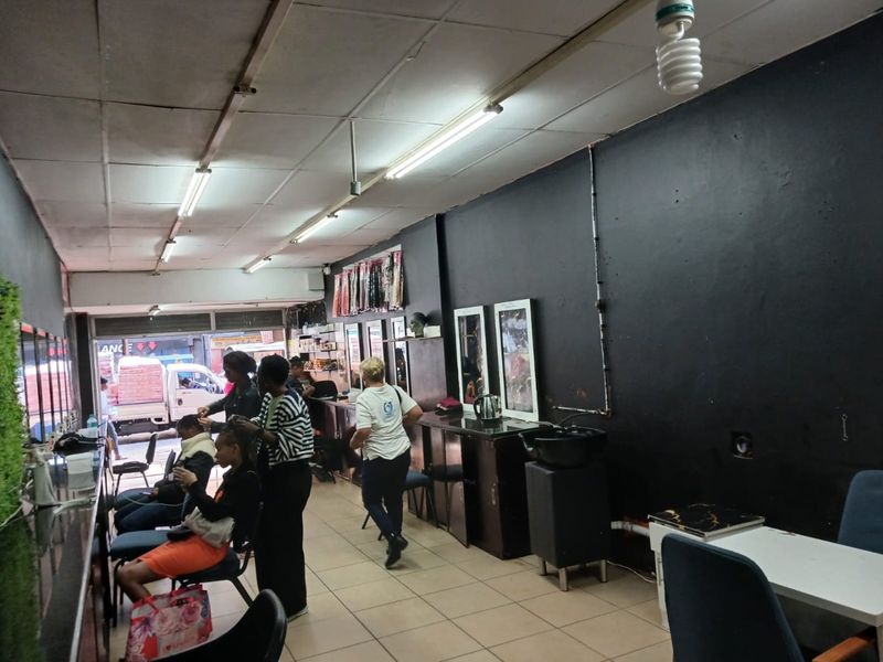 Commercial salon space featuring tiled flooring, drop ceiling, built-in vanity mirrors, and a plumbed wash basin, suitable for beauty or retail operations.