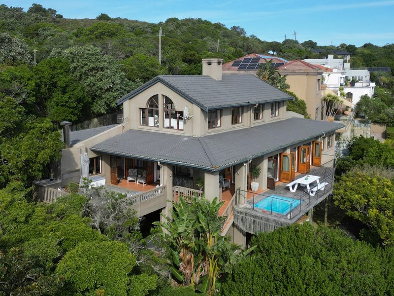 Aerial view of a multi-level house featuring a tiled roof, solar panels, and an elevated deck with a plunge pool set in a wooded area.