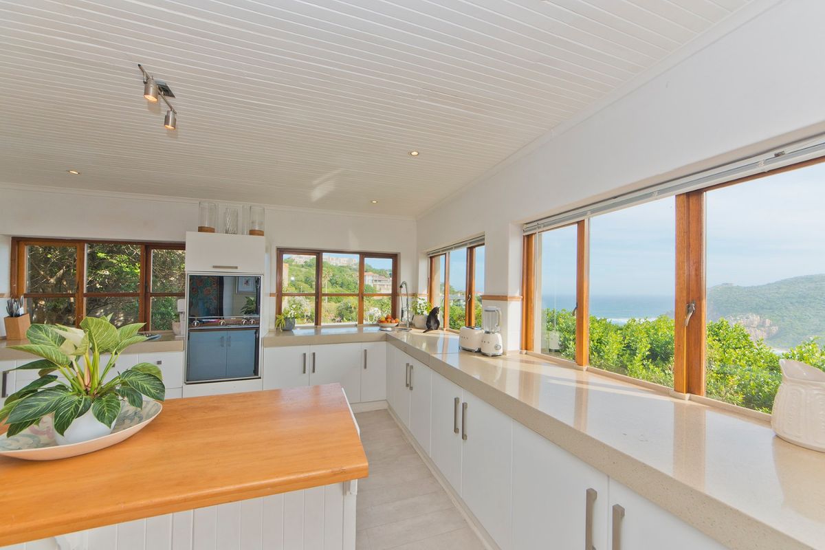 Bright kitchen featuring stone countertops, built-in oven, timber-framed windows, and a central island, offering scenic coastal views.