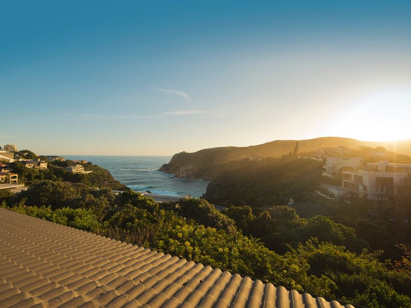 A scenic elevated view overlooking the coastal landscape, ocean, and surrounding residential properties at sunset.