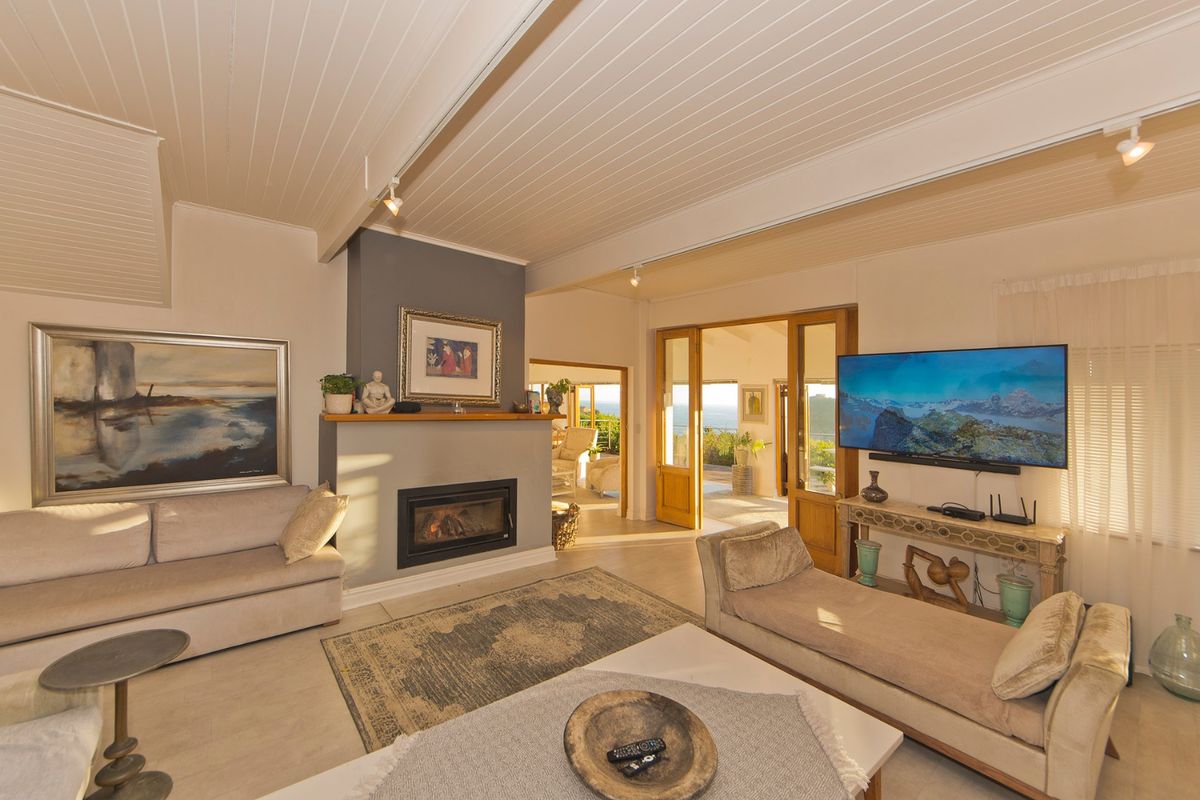 Spacious living room featuring a cozy fireplace, timber-lined ceiling, and large timber-framed glass doors opening to an outdoor area with scenic views.