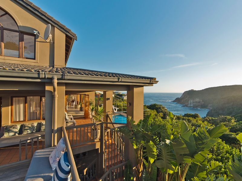 Spacious covered balcony featuring tiled flooring and railings, overlooking a swimming pool with stunning coastal and ocean views.