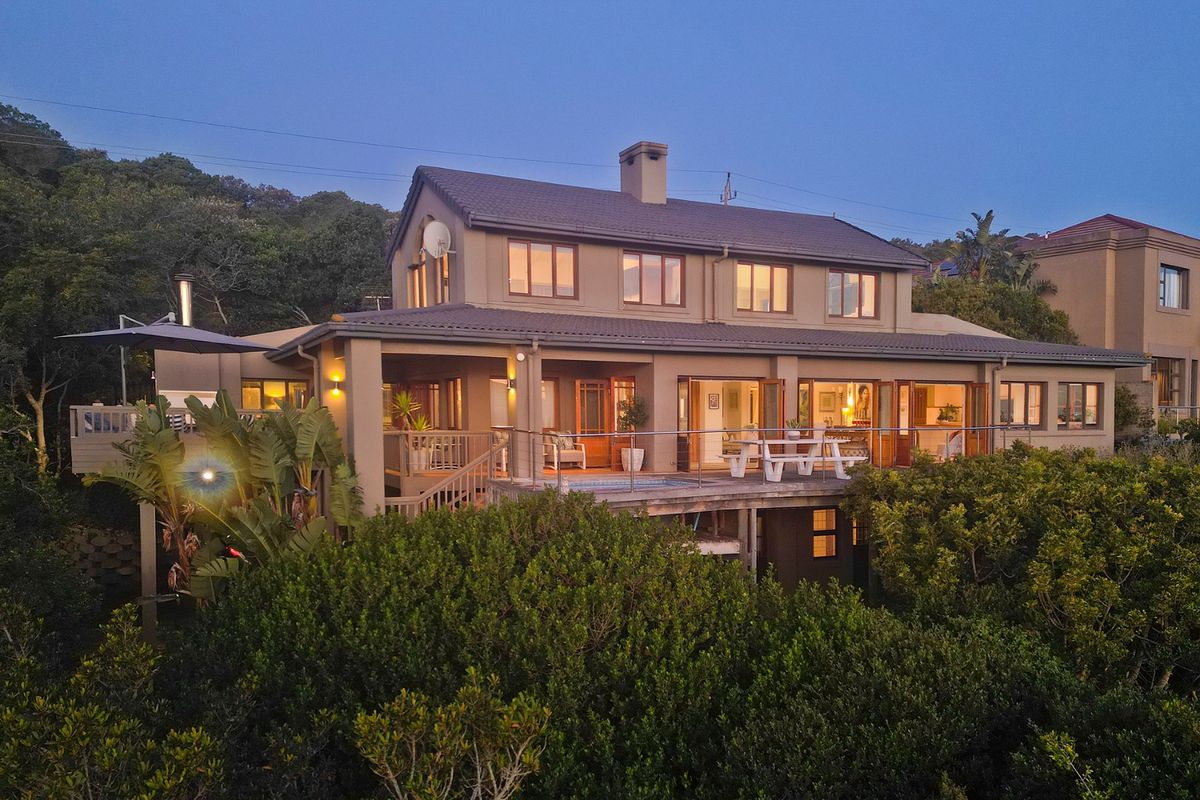 Rear elevation of a multi-story house featuring a spacious raised timber deck, integrated pool, and large sliding glass doors overlooking lush greenery.