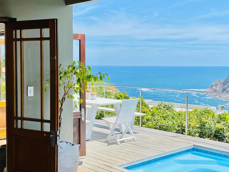 A scenic outdoor patio featuring timber decking, a stainless steel balustrade, and a swimming pool with expansive ocean views.