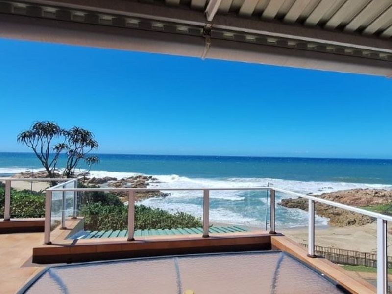 Spacious covered balcony featuring a glass balustrade and tiled flooring, offering expansive, unobstructed views of the coastline and ocean.