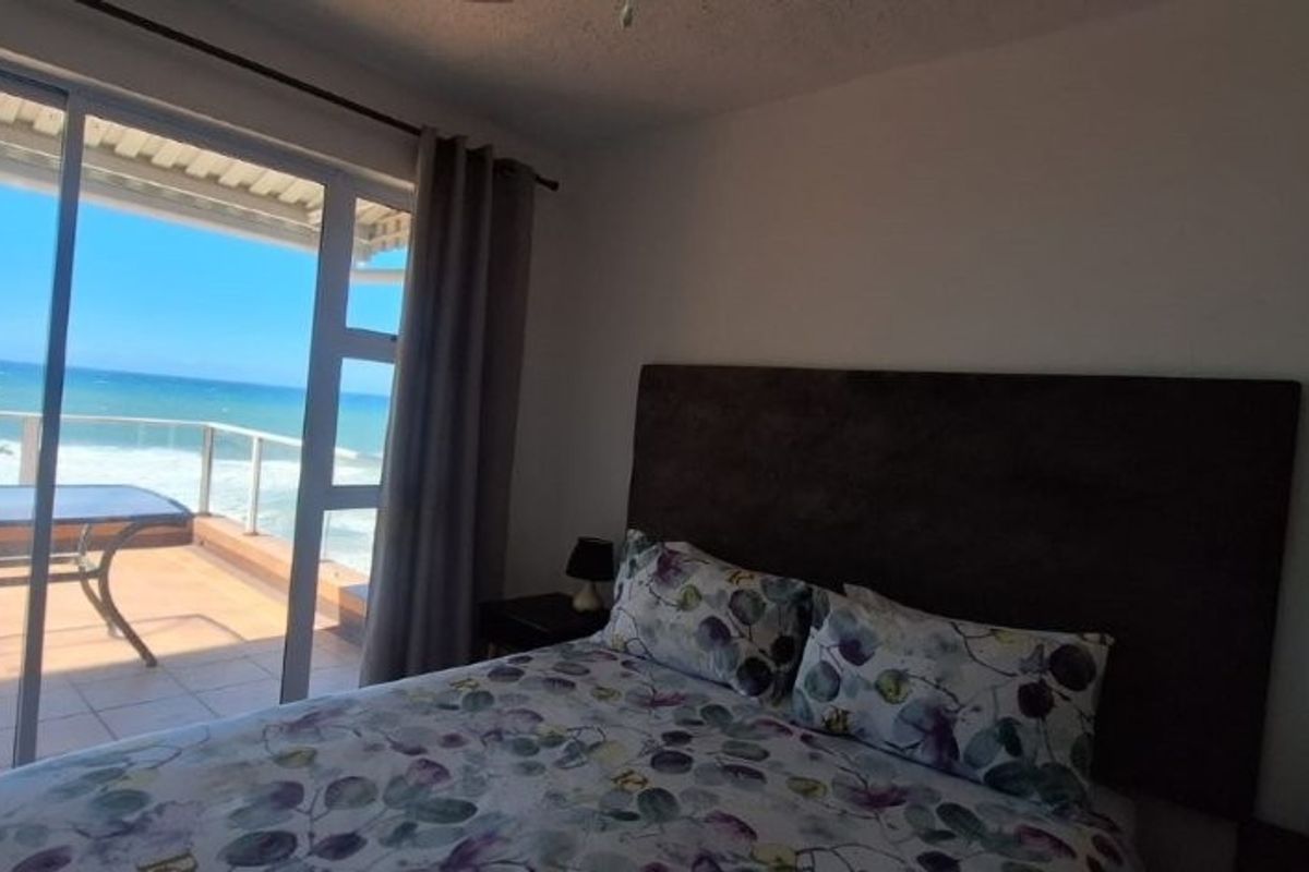 A bedroom featuring a large sliding glass door that opens onto a balcony with direct ocean views.
