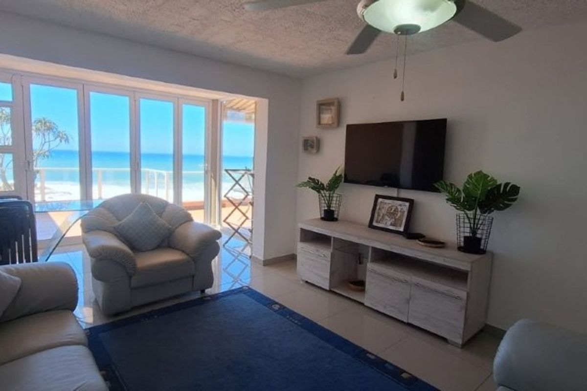 A bright living room featuring tiled flooring, a ceiling fan, and large sliding glass doors that provide direct access to a balcony with ocean views.
