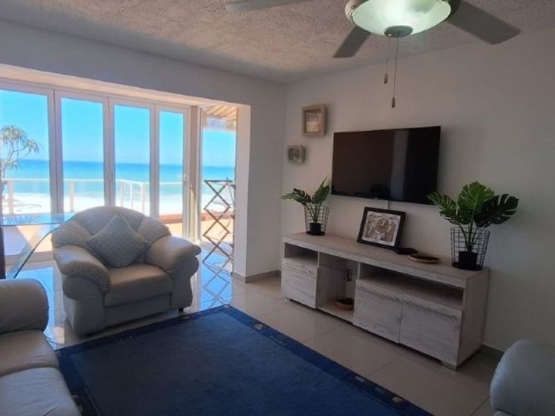 A bright living room featuring tiled flooring, a ceiling fan, and large sliding glass doors that provide direct access to a balcony with ocean views.