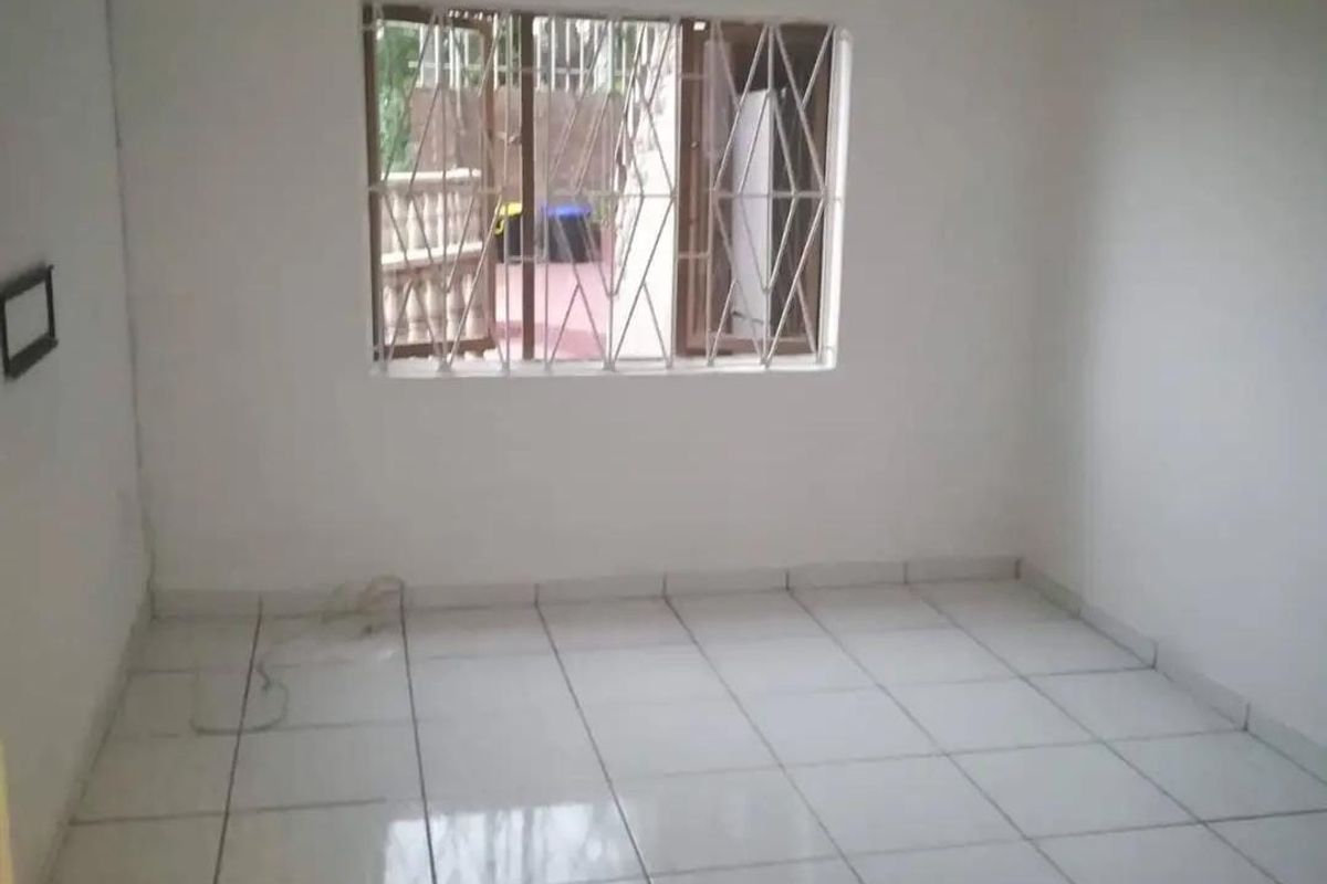 An empty bedroom featuring white walls, tiled flooring, and a window fitted with security bars.