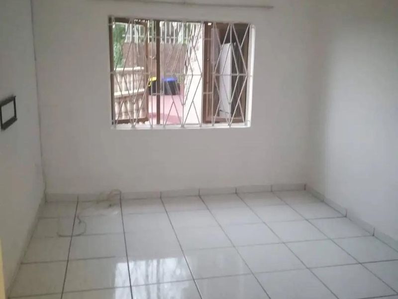 An empty bedroom featuring white walls, tiled flooring, and a window fitted with security bars.