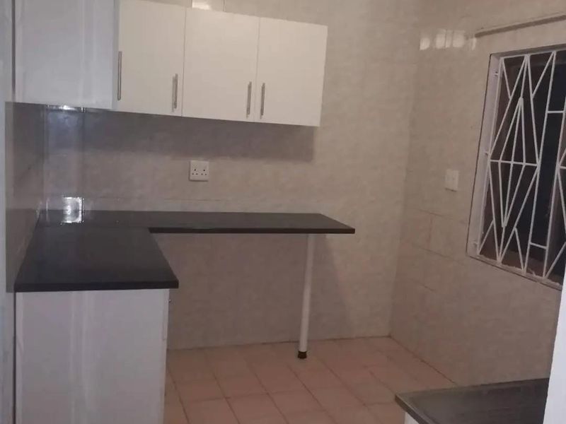 A functional, empty kitchen featuring white built-in cabinetry, dark countertops, tiled walls, and tiled flooring with a security-barred window.