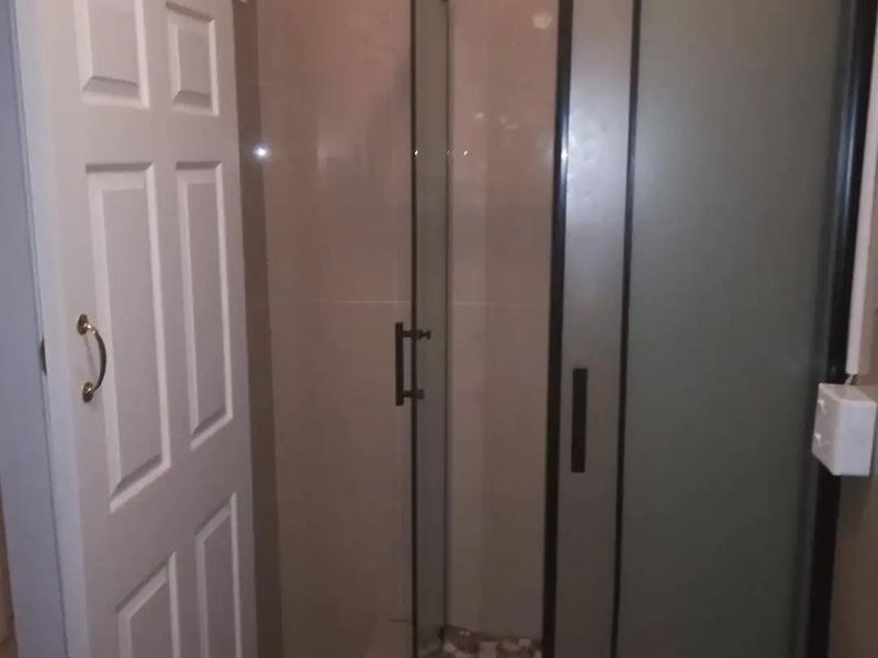 A compact bathroom featuring a modern shower enclosure with a sliding door and neutral wall tiling.