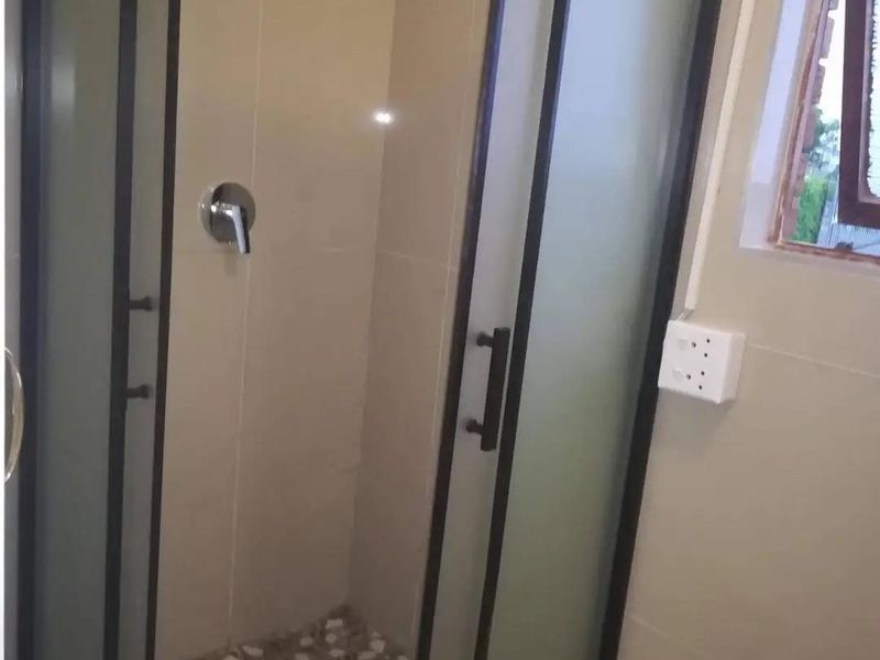 A modern bathroom shower featuring a glass enclosure, black frame, tiled shower floor, and neutral wall tiling.