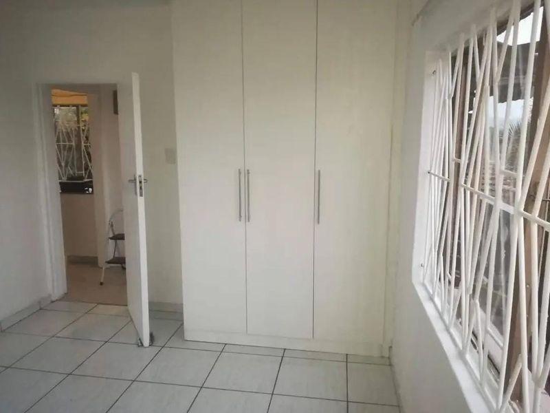 A clean, empty bedroom featuring white built-in cupboards, tiled flooring, and security bars on the window.