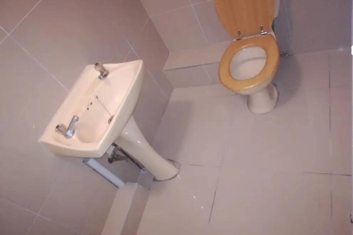 A compact bathroom featuring tiled walls and flooring, equipped with a pedestal basin and a standard toilet.