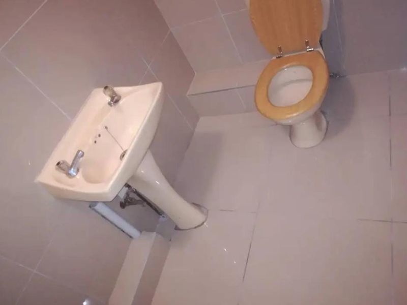 A compact bathroom featuring tiled walls and flooring, equipped with a pedestal basin and a standard toilet.