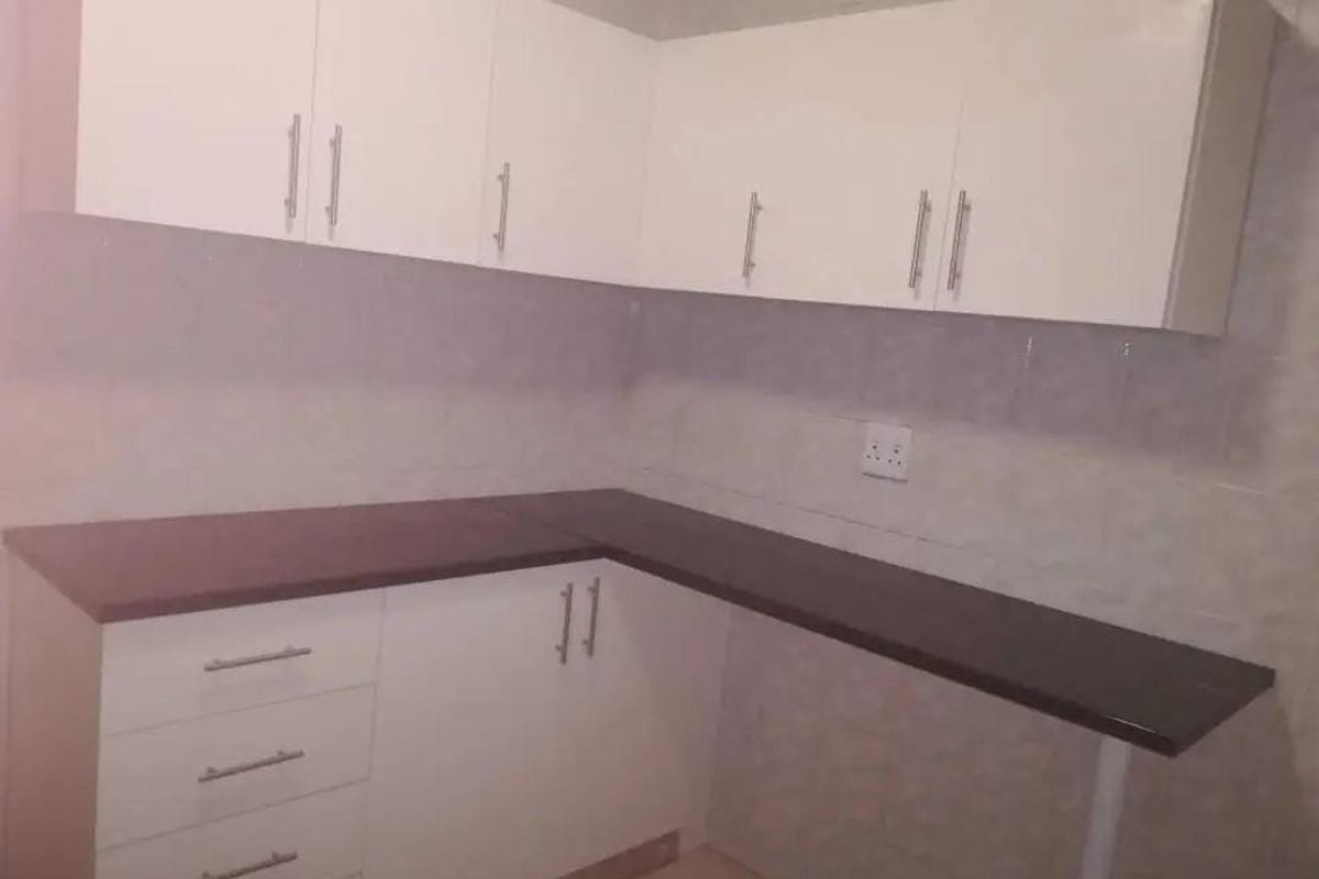 A clean, empty kitchen featuring white built-in cabinetry, dark laminate countertops, and a tiled backsplash.
